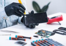 Kas geriausiai tvarko iPhone ekranus Vilniuje? iPhone ekranų remontas atliekamas servise – meistras su pirštinėmis ruošiasi pakeisti suskilusį telefono ekraną.