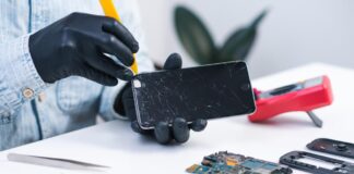 iPhone ekranų remontas atliekamas servise – meistras su pirštinėmis ruošiasi pakeisti suskilusį telefono ekraną.