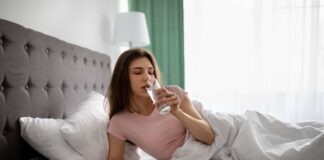 Stiklinė vandens prie lovos ryte gerdama moteris
