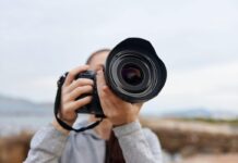 Vestuvių fotografijos stiliai: nuo klasikinio iki dokumentinio pasakojimo Vestuvių fotografijos stiliai – fotografas laiko profesionalią kamerą su dideliu objektyvu.