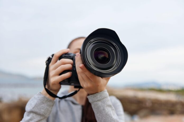 Vestuvių fotografijos stiliai – fotografas laiko profesionalią kamerą su dideliu objektyvu.