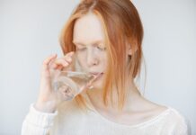 5 kūno signalai, kad skysčių geriama per mažai. Geriama per mažai skysčių. Mergina geria vandenį.