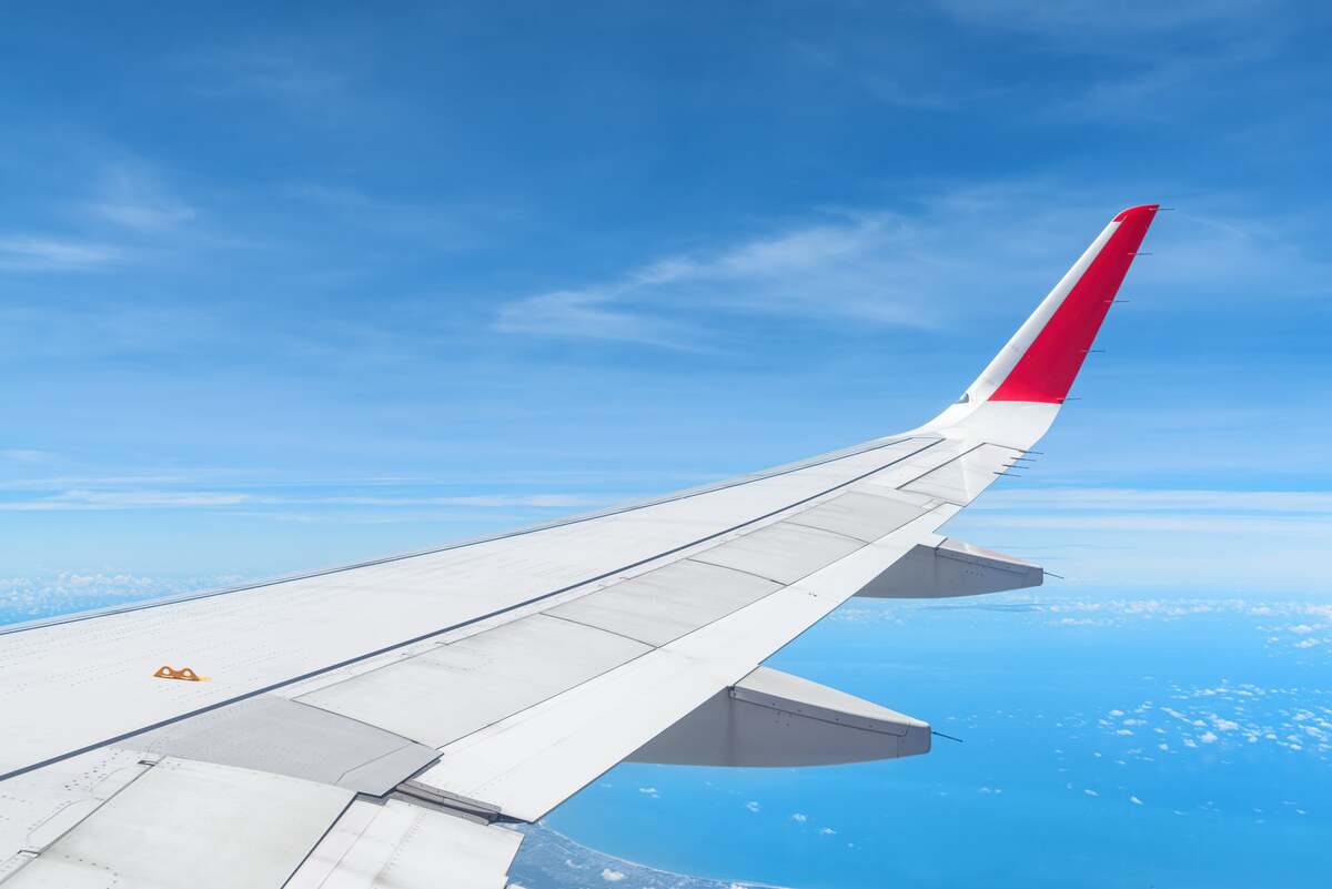 Kelionė į Turkiją matoma pro lėktuvo langą – sparnas virš debesų ir giedras dangus skrydžio metu.