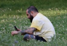 Telefonas daro daugiau įtakos nuotaikai nei manome Telefonas daro daugiau įtakos nuotaikai. Vyras sėdi pievoje ir žiūri telefoną.